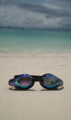 Fototapeta na wymiar Swim goggles on sandy beach over lagoon sea background. Travel, holiday, tropical vacation concept
