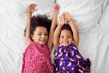 Two smiling little girls lying on bed with arms up