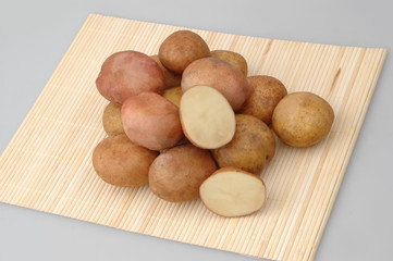 Lots of raw potatoes on bamboo stand on gray isolated background