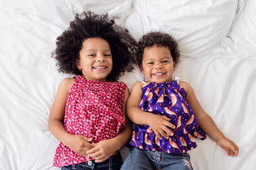 Two little girls lying on bed with big smile