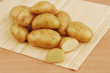 Lots of raw potatoes on bamboo stand on gray isolated background