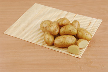Lots of raw potatoes on bamboo stand on gray isolated background