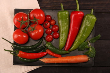 Vegetables, peppers, tomato, carrot, rosemary and spices over black plate and table.