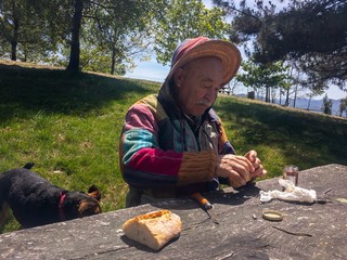 Mature man with hat, hood and colorful jacket, picnicking in a rest area with his dog.