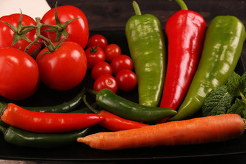 Vegetables, peppers, tomato, carrot, rosemary and spices over black plate and table.