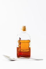 A vintage medicine bottle with cork filled with orange liquid and furnished with an empty label designed like a parchment roll with red sealing wax and a silver spoon on white background