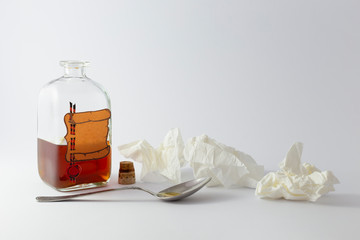 Arrangement of a spoon, handkerchiefs and a vintage medicine bottle with cork filled with orange liquid and furnished with an empty label like a parchment roll with red sealing wax on white background