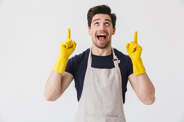 Photo of caucasian young man wearing yellow rubber gloves for hands protection pointing fingers at copyspace while cleaning house