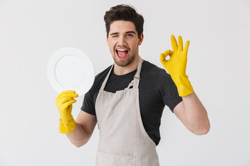 Photo of attractive young man wearing yellow rubber gloves for hands protection washing dishes...