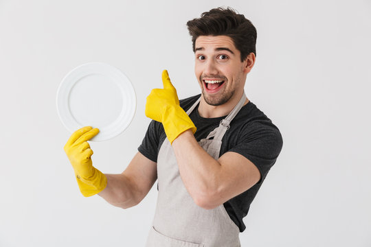 Photo of brunette young man wearing yellow rubber gloves for hands protection washing dishes while cleaning house