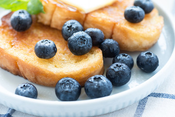 French toast with blueberries, honey and butter on a light plate. Sweet country breakfast.