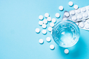 Pills and glass of water on blue top view.