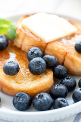 French toast with blueberries, honey and butter on a light plate. Sweet country breakfast.