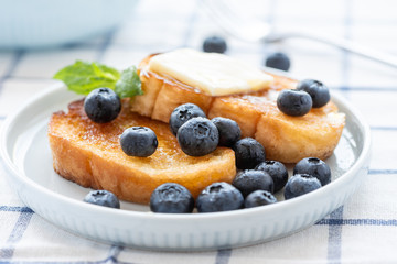French toast with blueberries, honey and butter on a light plate. Sweet country breakfast.