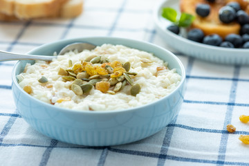 Sweet rice porridge, pudding, with raisins and pumpkin seeds in a blue bowl on the table. Delicious country breakfast.