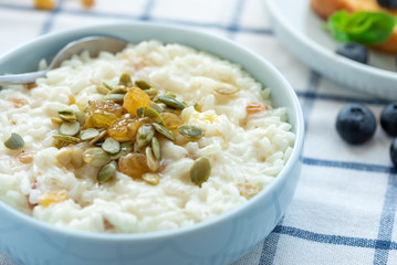 Sweet rice porridge, pudding, with raisins and pumpkin seeds in a blue bowl on the table. Delicious country breakfast.