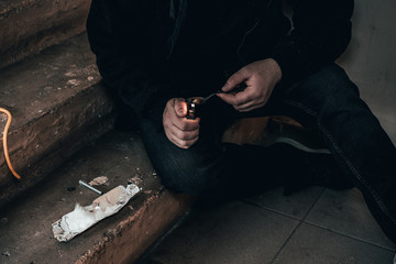 Young man addict with a syringe and heroin in the dirty basement (stairs). Drug addict. social issue