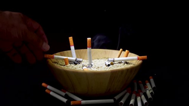 Many cigarettes are placed in a wooden cup of sand on a black background.
