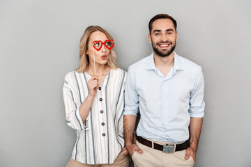 Photo closeup of happy couple in casual clothing having fun and holding paper fake glasses on stick