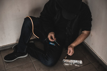 Young man addict with a syringe and heroin in the dirty basement (stairs). Drug addict. social issue