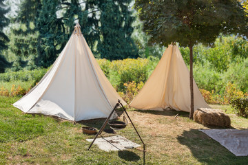 White tourist tent in forest camping on green trees summer sunny day background.