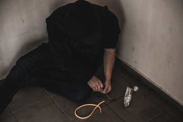 Young man addict with a syringe and heroin in the dirty basement (stairs). Drug addict. social issue