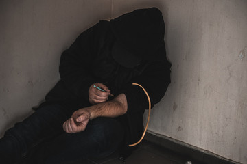 Young man addict with a syringe and heroin in the dirty basement (stairs). Drug addict. social issue