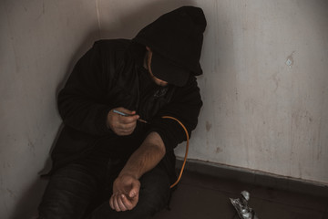 Young man addict with a syringe and heroin in the dirty basement (stairs). Drug addict. social issue