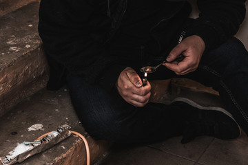 Young man addict with a syringe and heroin in the dirty basement (stairs). Drug addict. social issue