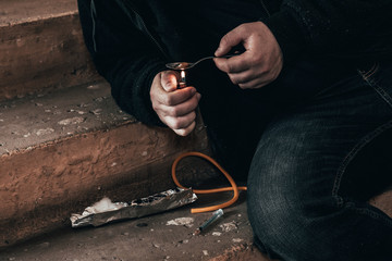 Young man addict with a syringe and heroin in the dirty basement (stairs). Drug addict. social issue