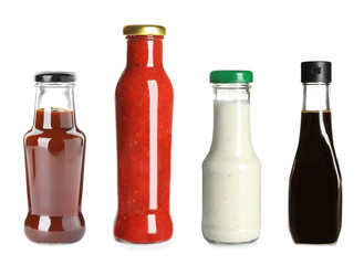 Set of glass bottles with different delicious sauces on white background