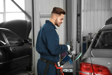 Technician polishing car body with tool at automobile repair shop