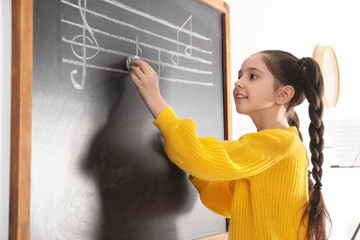 Little girl writing music notes on blackboard in classroom