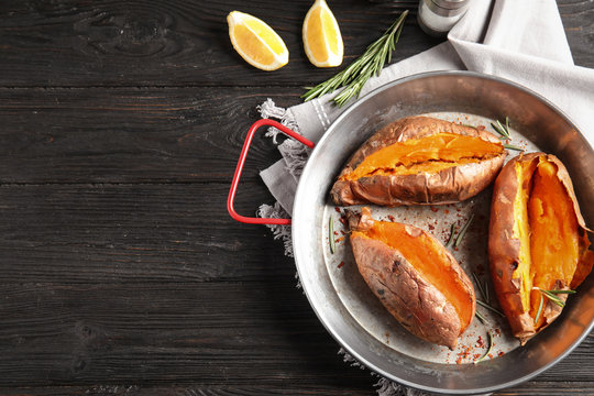 Flat lay composition with baked sweet potatoes in dish on wooden background. Space for text