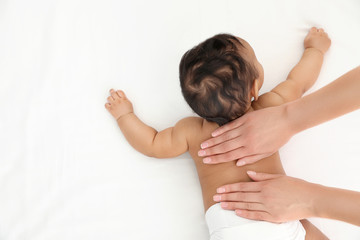 Top view of mother and her cute child on white bed, space for text. Baby massage and exercises