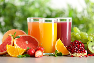 Three glasses with different juices and fresh fruits on table against blurred background