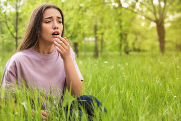 Young woman suffering from seasonal allergy outdoors, space for text