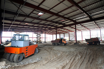 Fototapeta na wymiar At the construction site. View of a hangar building, an excavator and dump trucks loaded
