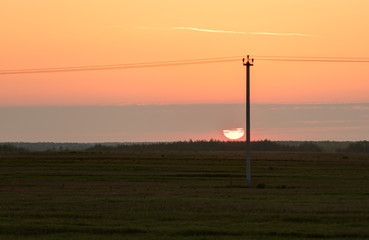 Fototapeta na wymiar Sunset with orange sky. Telegraph pole against the sun.
