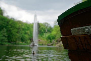 Old wooden boat stern on river and fountain behind