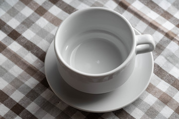 A white empty teacup stands on a table with a brown klechaty tablecloth