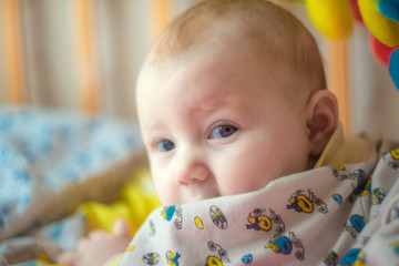 A newborn baby is lying in a baby bed and smiling, looking into the camera.