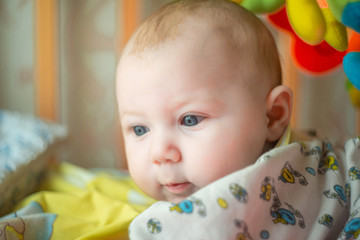 A newborn baby is lying in a baby bed and smiling, looking into the camera.
