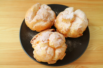 Plate of Three French Cream Puffs or Choux a la Creme Pastries Served on Wooden Table