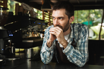 Portrait of attractive barista guy smiling while working in street cafe or coffeehouse outdoor