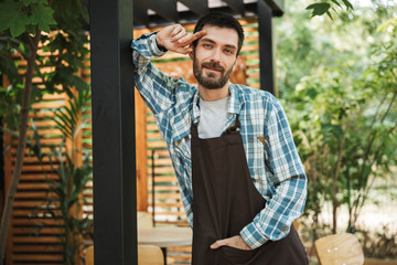 Obraz premium Portrait of young barista man smiling at camera while working in street cafe or coffeehouse outdoor