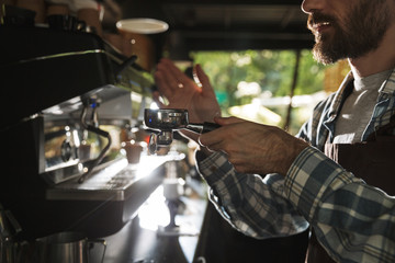 Image closeup of bearded barista man making coffee while working in cafe or coffeehouse outdoor