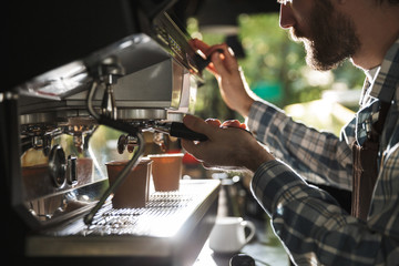 Image closeup of attractive barista man making coffee while working in cafe or coffeehouse outdoor