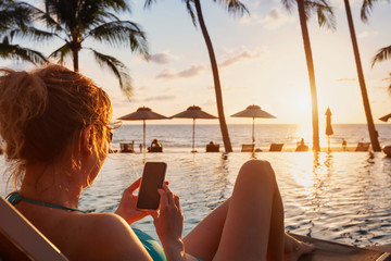woman using smartphone on beach luxury hotel near swimming pool, travel app for tourist on mobile...
