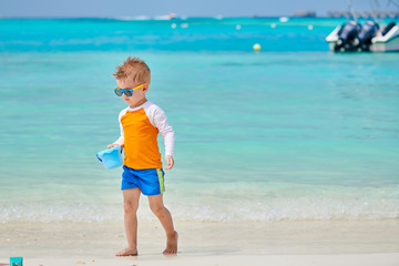 Fototapeta na wymiar Three year old toddler boy playing with beach toys on beach. Summer family vacation at Maldives.